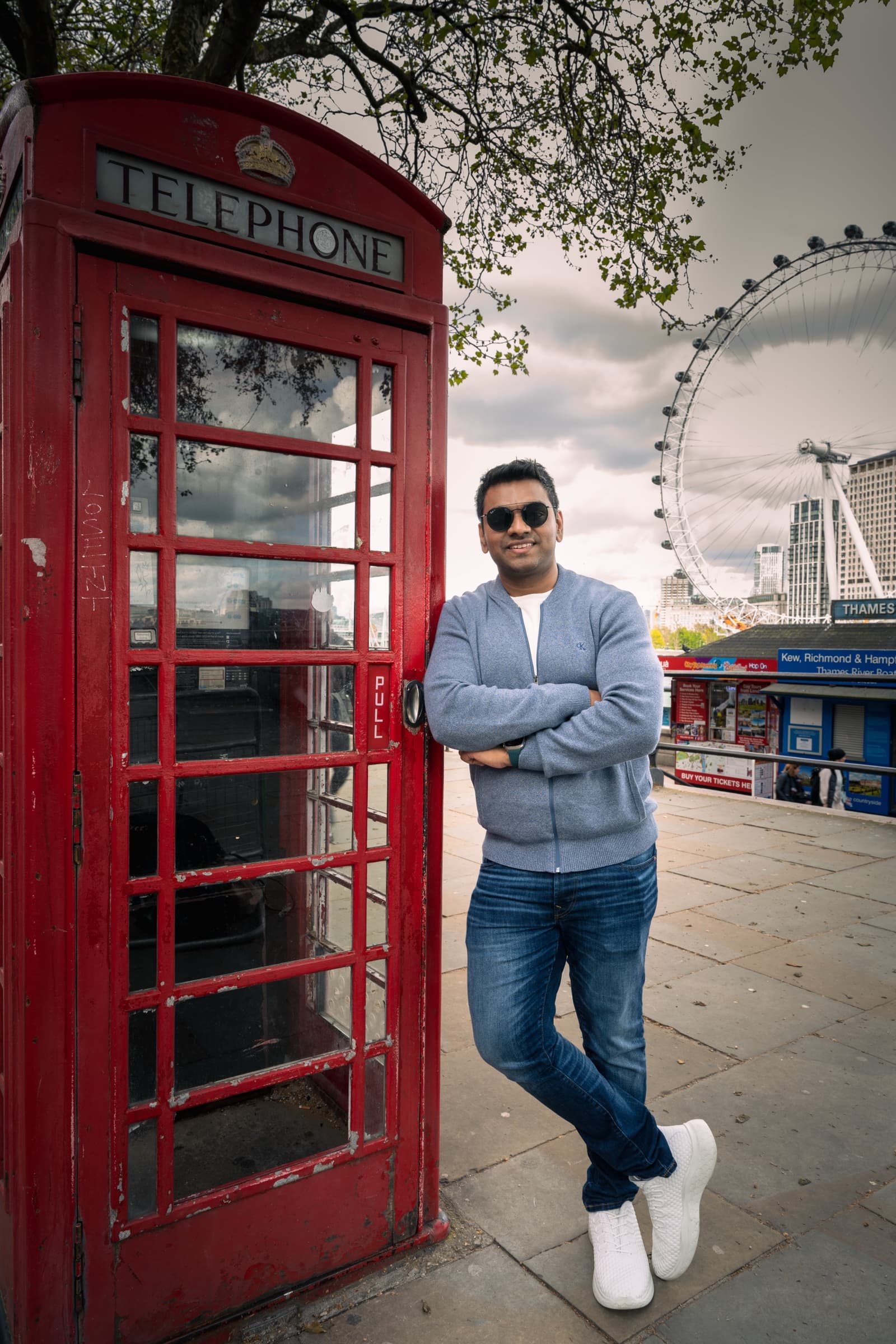 Avigit standing beside a red telephone box in London, arms crossed, smiling